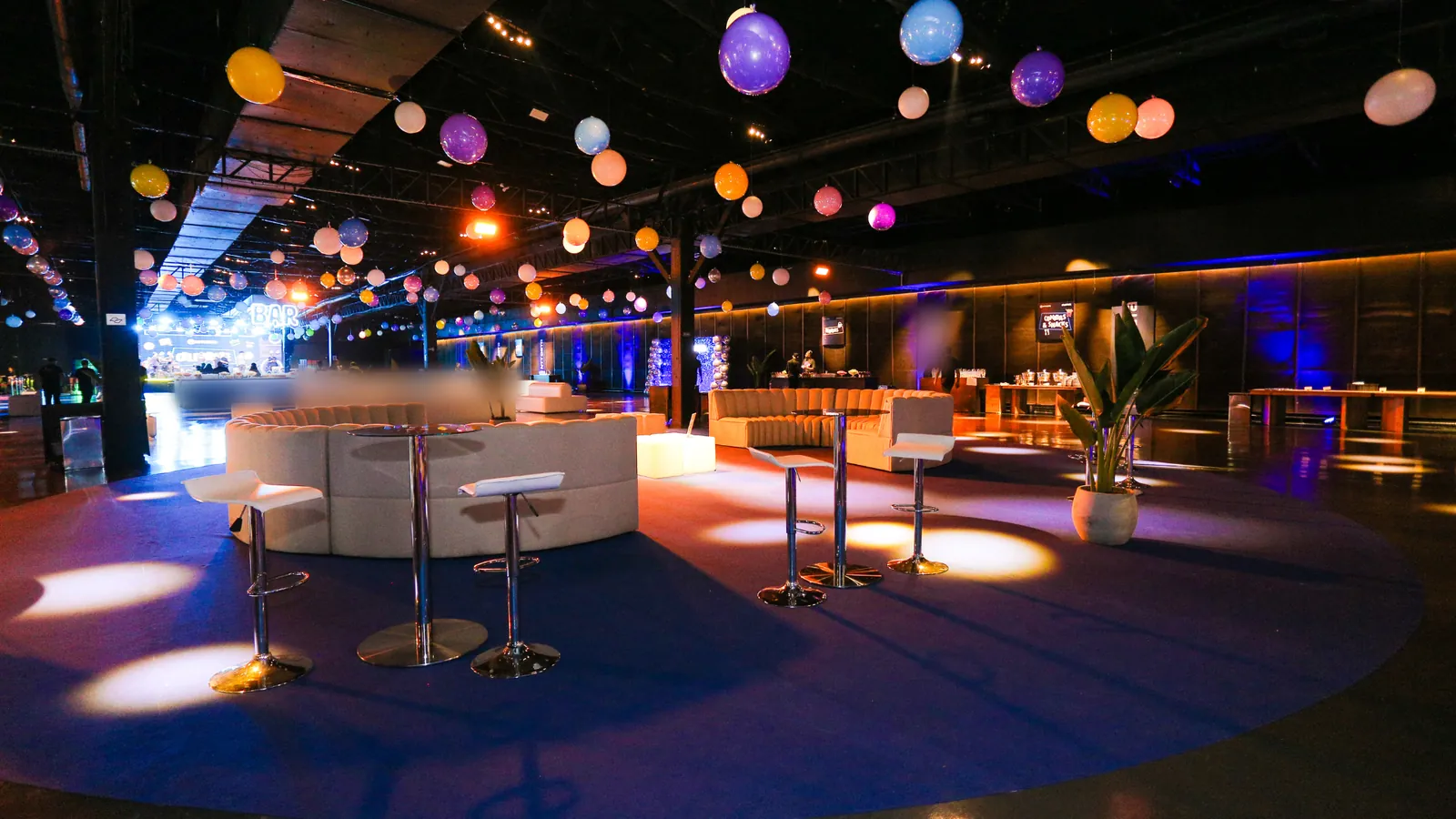Salão da Vila dos Ipês montado para evento, com lounges, mesas altas e iluminação cênica